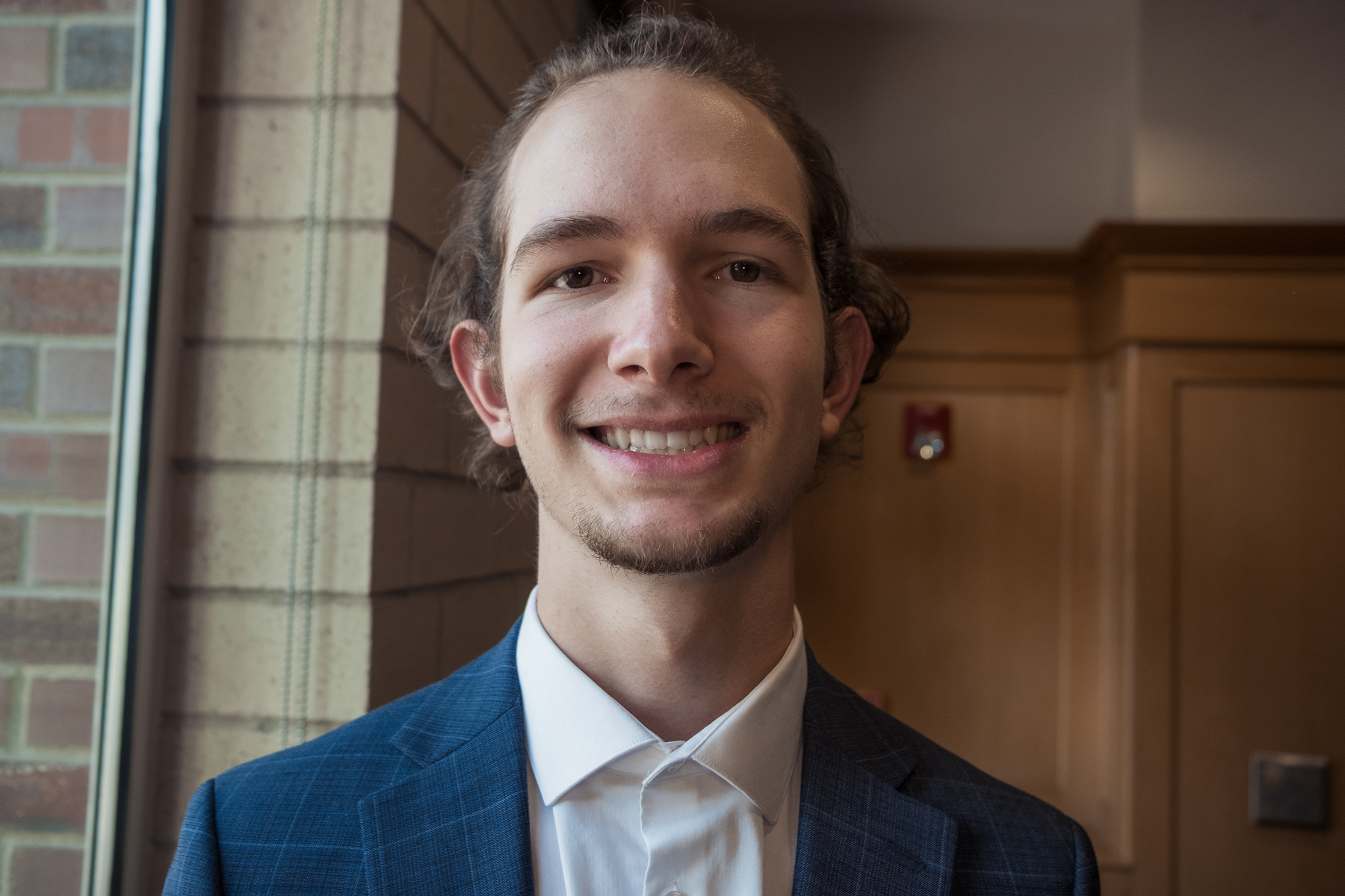 Professional headshot of a young man in a blue plaid suit